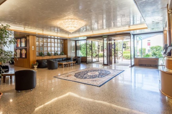 Elegancki hol w hotelu z kryształowym żyrandolem, dekoracyjnym dywanem i ladą recepcyjną.