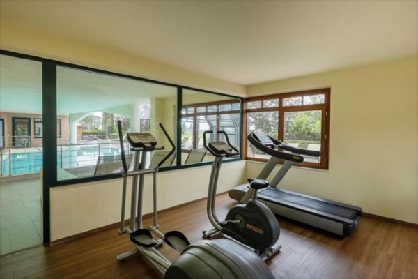 Pomieszczenie z wyposażeniem fitness i widokiem na kryty basen.