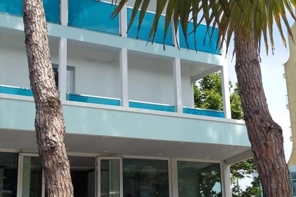 Nowoczesny budynek z niebieskimi szklanymi balustradami i drzewami na pierwszym planie.