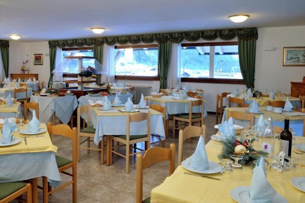 Przestronna restauracja z wieloma stolikami przygotowanymi dla gości, ozdobiona jasnoniebieskimi i żółtymi obrusami.