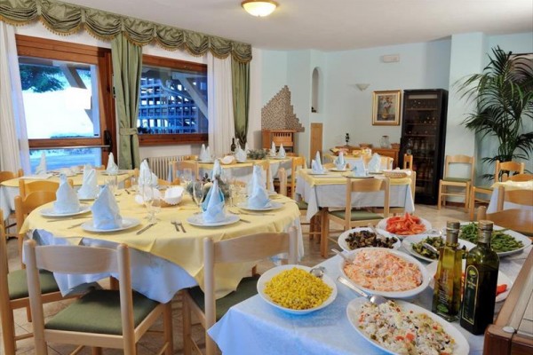 Restauracja z kilkoma stolikami przygotowanymi dla gości, na stole na pierwszym planie różne sałatki i oliwy z oliwek.
