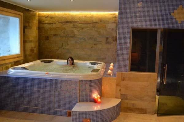 Osoba relaksująca w jacuzzi obok oświetlonej sauny i świec.