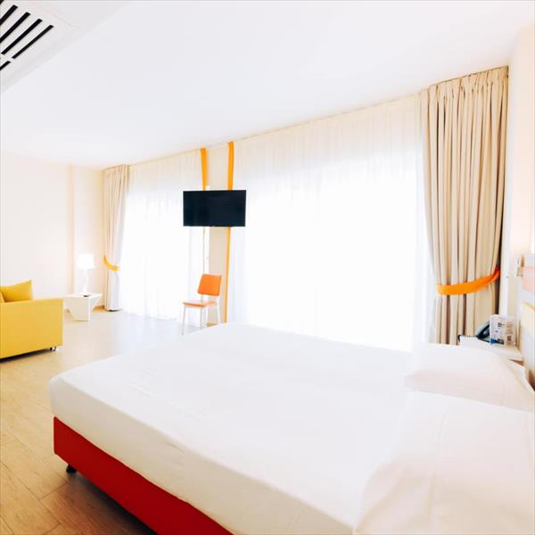 Jasny pokój hotelowy z dużym łóżkiem, żółtą kanapą i telewizorem na ścianie.