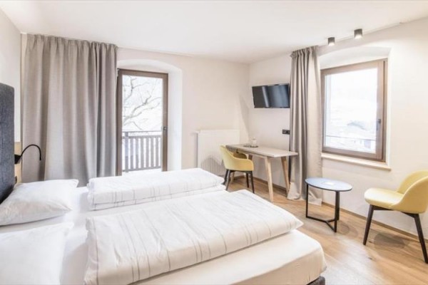 Jasny pokój hotelowy z dwoma łóżkami, biurkiem, krzesłem i balkonem.