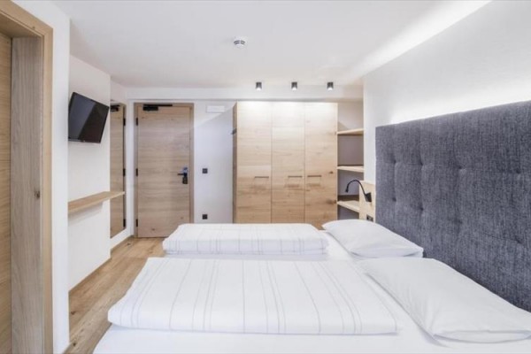 Nowoczesny pokój hotelowy z podwójnym łóżkiem, telewizorem i drewnianymi meblami.