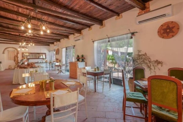 Wnętrze restauracji z drewnianym sufitem, okrągłymi stołami i dużymi oknami.