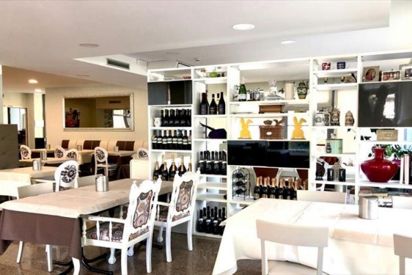 Stylowa restauracja z białymi meblami i półkami pełnymi butelek wina.