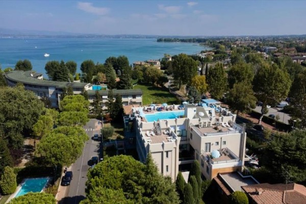 Widok na hotel z basenem na dachu przy jeziorze otoczony drzewami i innymi budynkami.