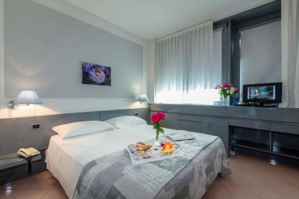 Pokój hotelowy z podwójnym łóżkiem, na którym znajduje się taca ze śniadaniem.