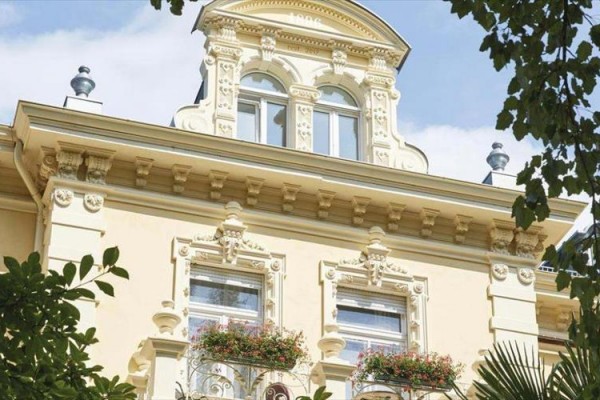 Zabytkowy budynek z bogato zdobioną fasadą i kwiatową dekoracją na balkonach.