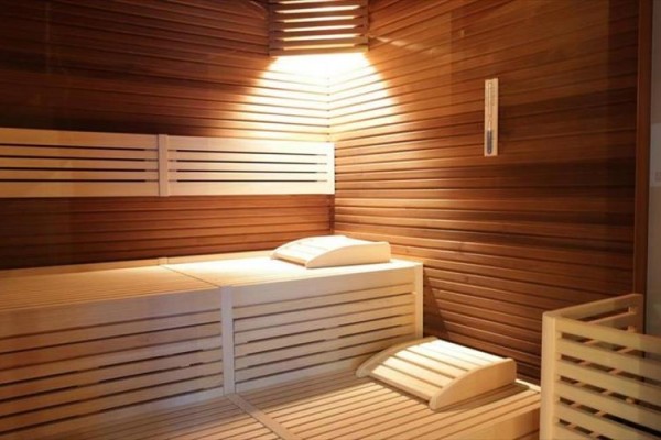 Drewniana sauna z ławką i poduszkami oświetlona od góry.