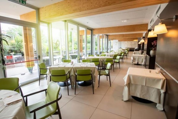 Nowoczesna restauracja ze szklanymi ścianami i zielonymi krzesłami.