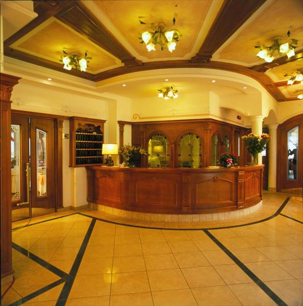 Recepcja hotelowa z drewnianym kontuarem i dekoracją kwiatową.