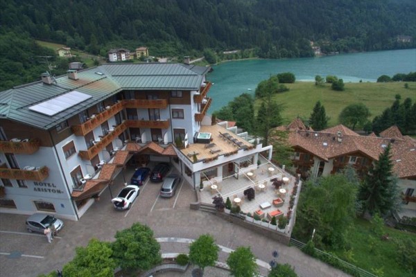 Hotel z tarasem i parkingiem nad jeziorem w górskim krajobrazie.