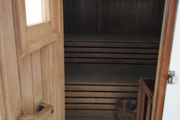 Otwarta drewniana sauna z ławką i małym wiadrem wewnątrz.