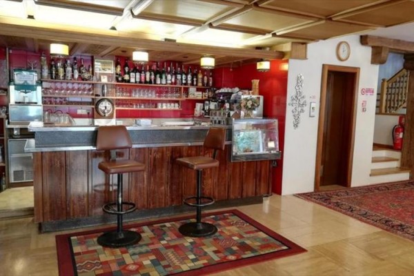 Bar z drewnianym blatem, dwoma krzesłami i regałem z butelkami i szklankami.