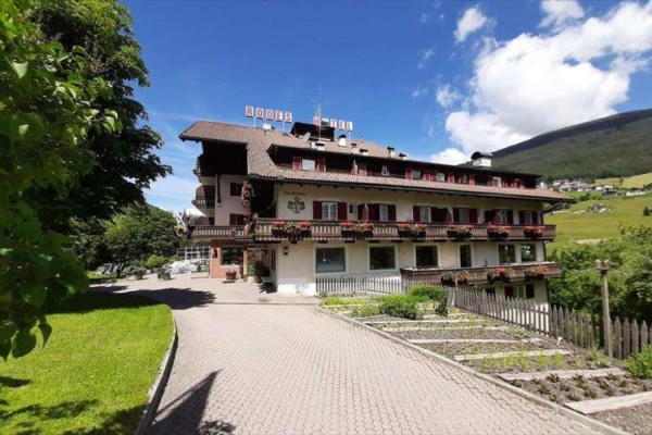 Hotel z ozdobnymi balkonami otoczony zielenią i wzgórzami w słoneczny dzień.