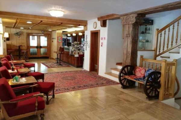 Hol hotelowy z czerwonymi fotelami, drewnianymi schodami i ozdobnym wózkiem.