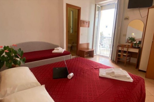 Pokój z czerwonymi łóżkami, otwartym laptopem, balkonem i toaletką.