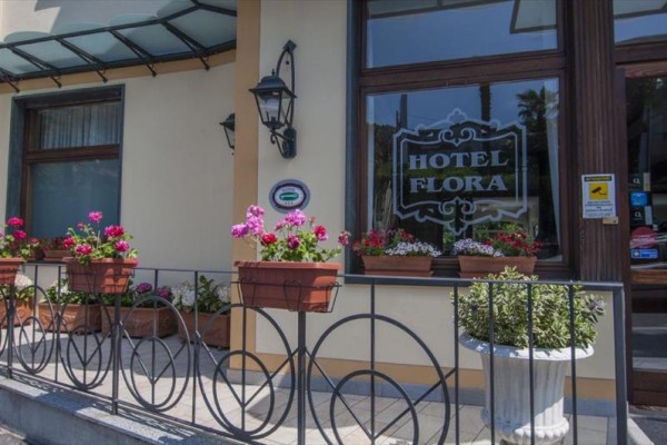 Wejście do hotelu Flora z kwiatami na balustradzie i parapecie okiennym.