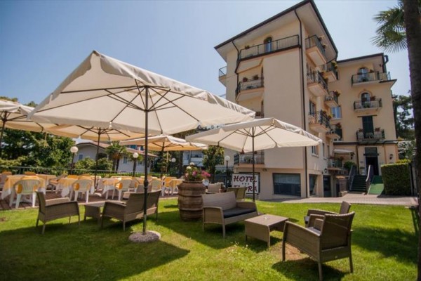 Zewnętrzne siedzenie z rattanowymi meblami i parasolami przed budynkiem hotelowym.