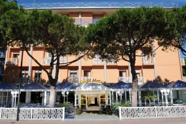 Wejście do hotelu z pomarańczową fasadą, otoczone drzewami i niebieskimi markizami.