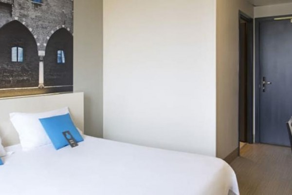 Nowoczesny pokój hotelowy z białym łóżkiem, niebieskimi poduszkami i dekoracją ścienną z łukami.