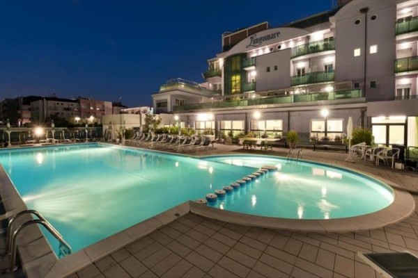 Nocny widok na oświetlony hotel z zewnętrznym basenem.