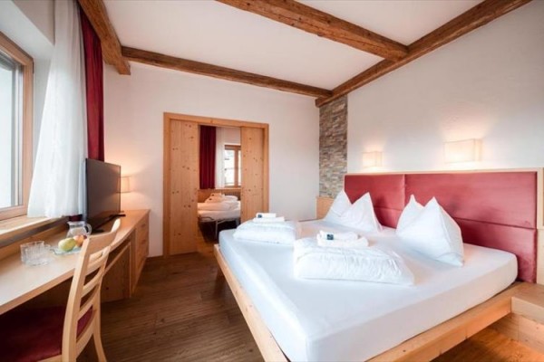 Nowoczesny pokój hotelowy z podwójnym łóżkiem, drewnianymi meblami i telewizorem przy oknie.