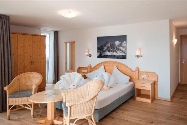 Pokój hotelowy z łóżkiem małżeńskim, wiklinowymi fotelami i drewnianymi meblami.