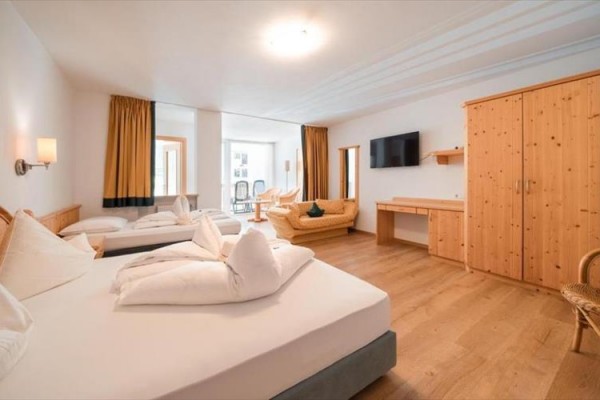 Przestronny pokój hotelowy z łóżkiem małżeńskim, szafą, telewizorem i tapicerowaną sofą.