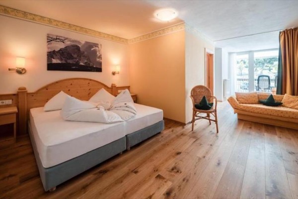 Jasny pokój hotelowy z łóżkiem małżeńskim, rozkładaną sofą i drewnianą podłogą.