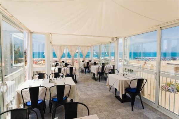 Restauracja z widokiem na plażę i morze za przeszklonymi ścianami.