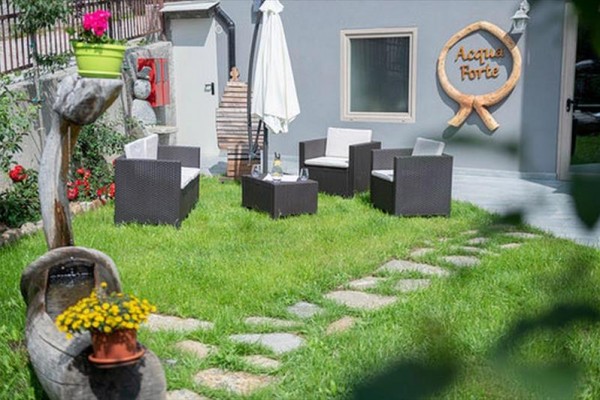 Ogródkowe siedzenie z rattanowymi fotelami i parasolem na trawniku przed szarym budynkiem z napisem 