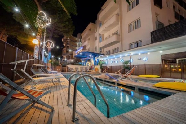 Zewnętrzny basen hotelowy z leżakami i oświetleniem nocnym.