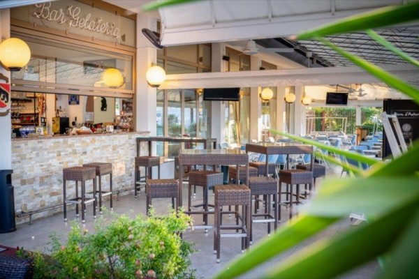 Zewnętrzny bar z wysokimi stolikami i krzesłami, ozdobiony lampami i roślinami.