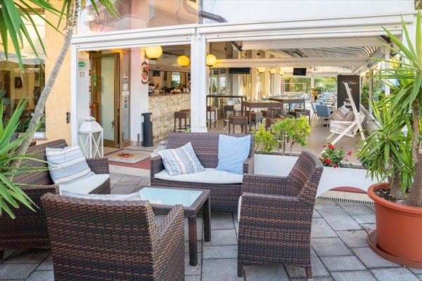 Zewnętrzny taras z meblami ratanowymi i poduszkami przed otwartą restauracją.