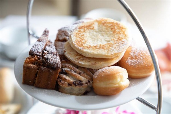 Talerz pełen różnych słodkich deserów, takich jak naleśniki, ciasta i pączki, posypanych cukrem.