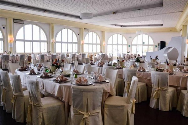 Elegancko nakryta sala jadalna z okrągłymi stołami i białymi pokrowcami na krzesłach.