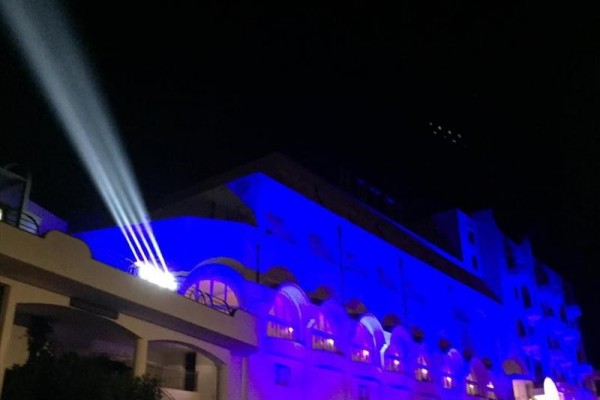 Budynek oświetlony niebieskimi światłami z reflektorem rzutującym światło na niebo w nocy.