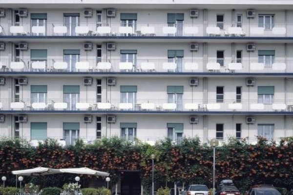 Biały budynek hotelu z balkonami porośniętymi pnączami.