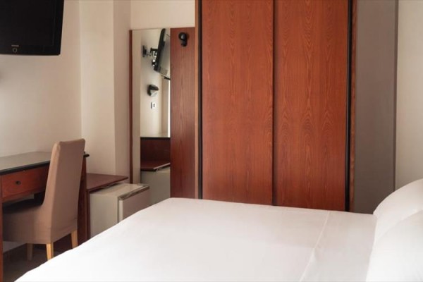 Nowoczesny pokój hotelowy z białą pościelą, drewnianą szafą i biurkiem.