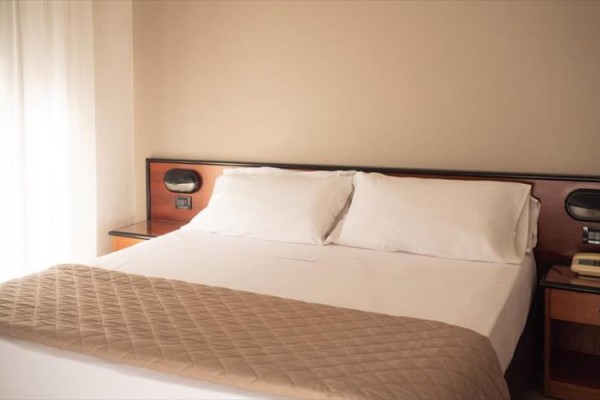 Łóżko małżeńskie z białą pościelą w prostym pokoju hotelowym.