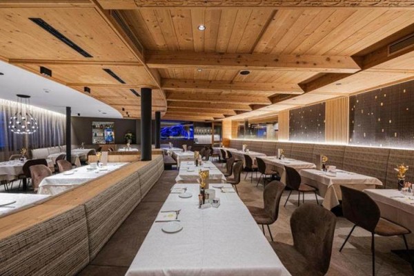 Nowoczesna restauracja z drewnianym sufitem i stolikami nakrytymi białymi obrusami.