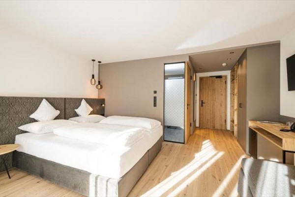 Nowoczesny pokój hotelowy z dużym łóżkiem, telewizorem i drewnianą podłogą.