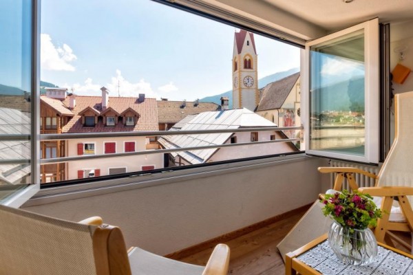 Balkon z widokiem na dachy domów i wieżę kościoła.