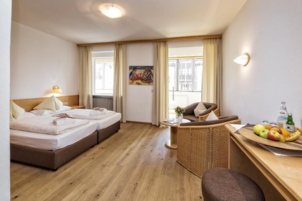 Jasny pokój hotelowy z podwójnym łóżkiem, miejscem do siedzenia i biurkiem z owocami.