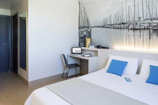 Nowoczesny pokój hotelowy z łóżkiem dwuosobowym i fotografią jachtów na ścianie.