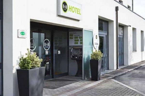 Wejście do nowoczesnego hotelu z automatycznym terminalem recepcyjnym i donicami.