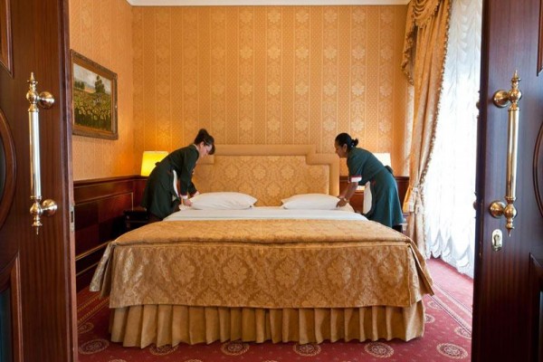 Dwie pokojówki ścielą łóżko małżeńskie w luksusowym pokoju hotelowym.